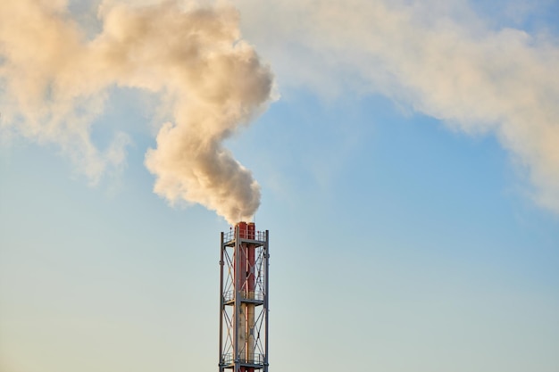 Smoke exhausting from chimney. Huge smoke from the pipe. Red-white chimney of factory. Environmental pollution. Carbon dioxide emissions. Global climate protection concept.