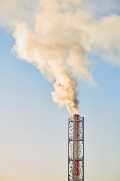 Smoke exhausting from chimney. Huge smoke from the pipe. Red-white chimney of factory. Environmental pollution. Carbon dioxide emissions. Global climate protection concept.