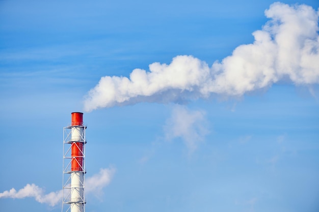 Smoke exhausting from chimney. Huge smoke from the pipe. Red-white chimney of factory. Environmental pollution. Carbon dioxide emissions. Global climate protection concept.