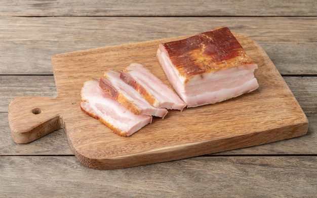 Smoked bacon with slices and knife over wooden board.