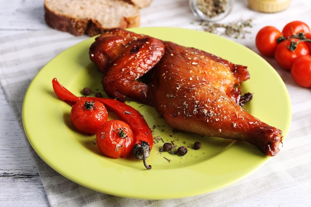 Smoked chicken leg with vegetables on plate on table close up