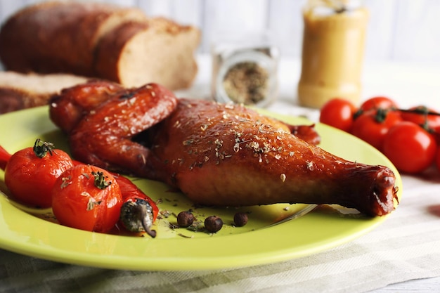 Smoked chicken leg with vegetables on plate on table close up