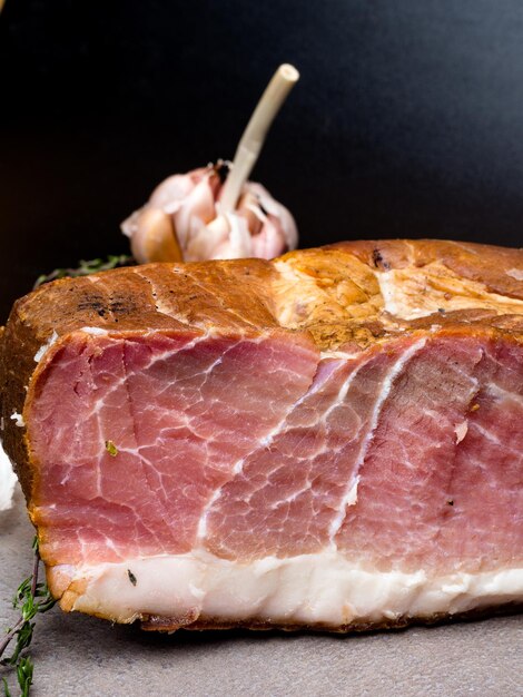 Smoked ham on a stone table with addition of fresh aromatic herbs and spices Natural product from organic farm produced by traditional methods