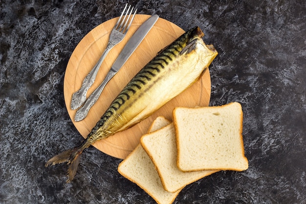 Smoked mackerel without head with fork knife cutting board bread 