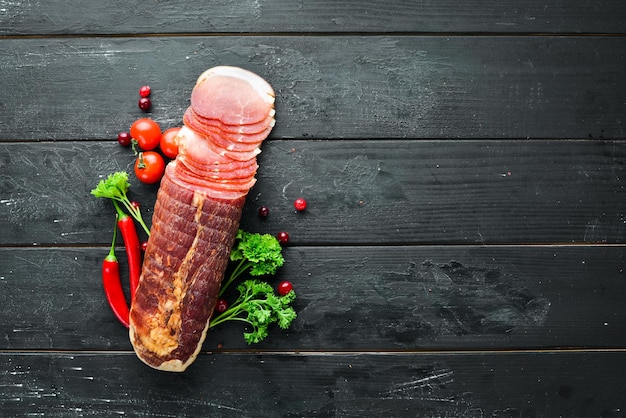 Smoked meat with spices and herbs. On a black wooden background. Top view. Free space for your text.