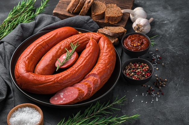 Smoked sausage with sliced on a dark background with bread, sauce and rosemary. Side view, copy space.