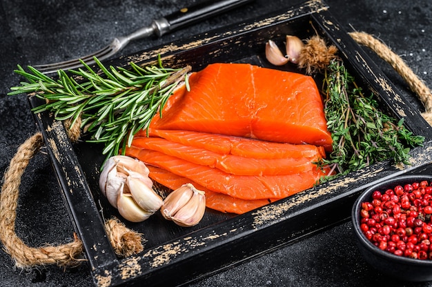 Smoked sliced salmon fillet in a wooden tray with herbs on wooden table. Top view.