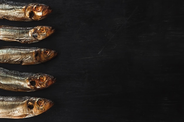 Smoked sprat fish golden brown on a black background with space for text