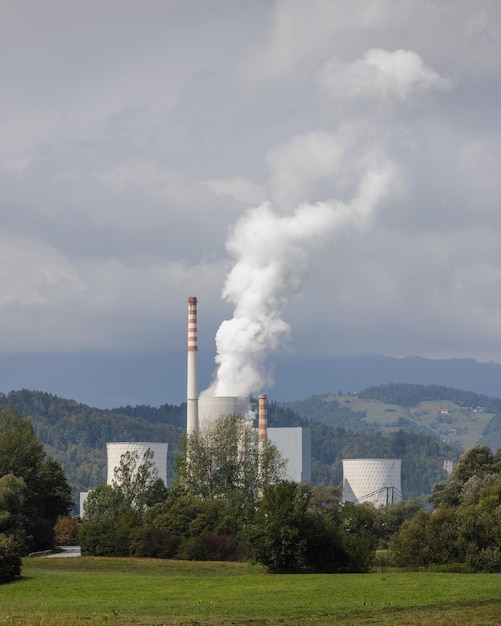 Smoking chimney at thermal power plant near lake and green nature