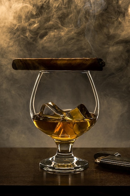 Smoking Cuban Cigar on Top of Elegant Whisky Glass with Ice Cubes Copy Space Background