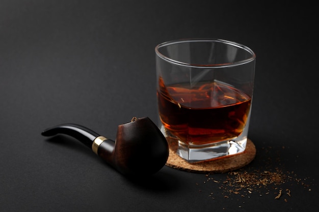 Smoking pipe tobacco and glass of alcohol on black background