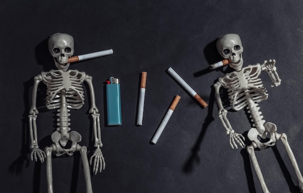 Smoking skeletons with cigarette in the mouth against black dark background. Smoking kills