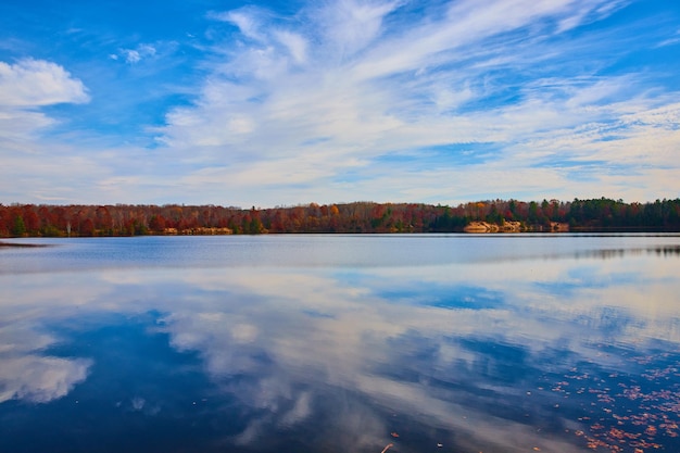 Smooth lake reflecting blue sky and fall trees lining the coast