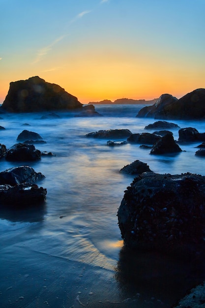 Smooth waves around rocks on beach at golden hour in California