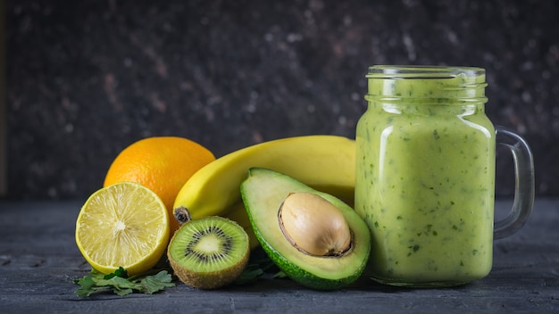 Smoothie of avocado, banana, kiwi and lemon on a wooden table against a black wall Vegetarian food for a healthy lifestyle