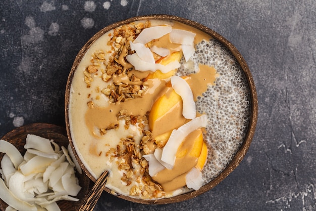 Smoothie bowl with chia pudding, peach, coconut and granola in a coconut bowl. 