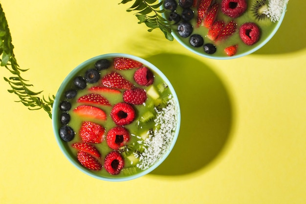 smoothie bowl with fresh berries and fruits in blue plate on yellow dark shadow. High quality photo