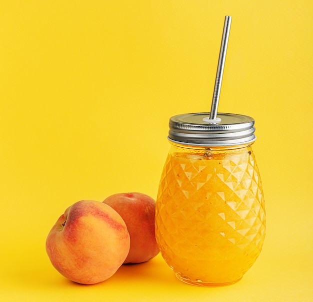 Smoothie jar of ripe juicy peaches on yellow wall.