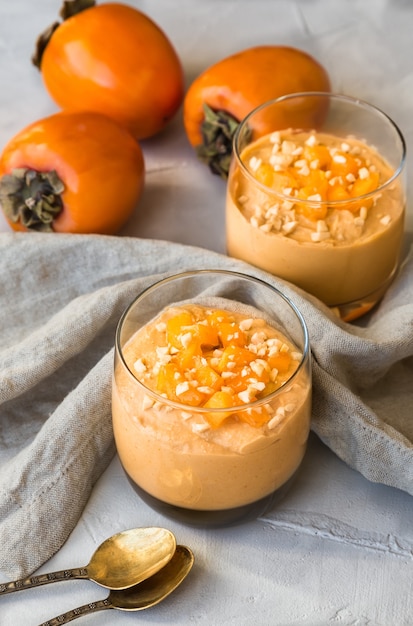 Smoothie with persimmon and cashew nuts in glasses on gray concrete