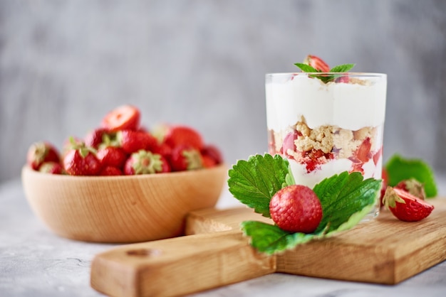 Smoothie with summer strawberry in glass jar and fresh berries in wooden bowl on a gray background