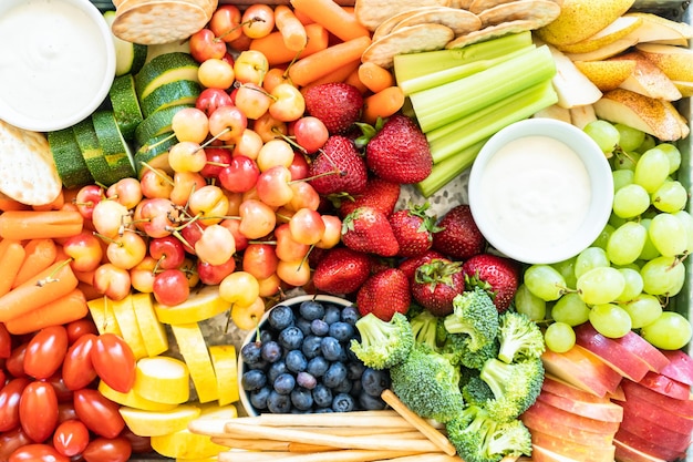 Snack board with fresh fruit, vegetables, crackers, and dips.