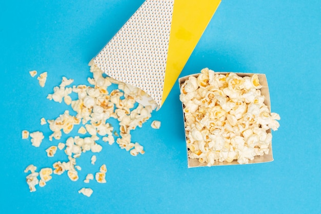 Snack concept Sweet popcorn in paper cup and spill out from paper cup on light blue background