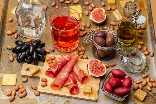 Snack food Jamon and figs on board Olives in glass jars Glass of rose wine and sprig of grapes