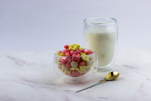 Snacks with raspberry and banana flavor in the shape of hearts and flowers A bowl with a quick breakfast and a glass of milk on a white background