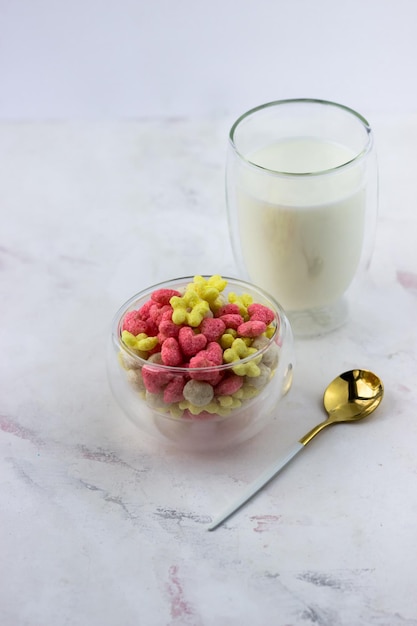 Snacks with raspberry and banana flavor in the shape of hearts and flowers A bowl with a quick breakfast and a glass of milk on a white background