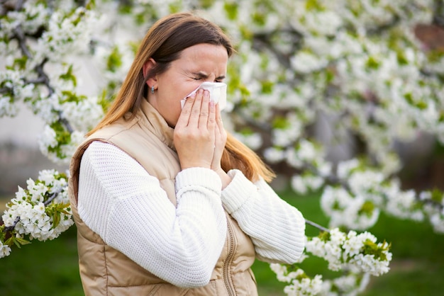 Sneezing woman with a nose wiper among the flowering trees in the park