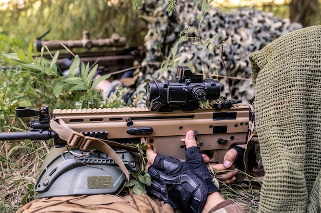 Snipers under camouflage nets lying in ambush and pointing rifles at enemy