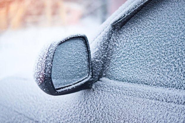 Snow covered car parked outside Closeup of frozen rear view mirror