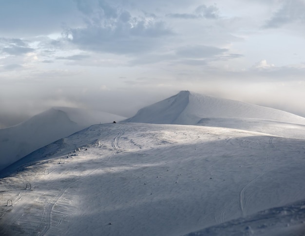 Snow covered mountain slope in last evening sunlight Magnificent windy dusk on tops above picturesque alpine ski resort Dragobrat Ukraine Carpathian Mountains