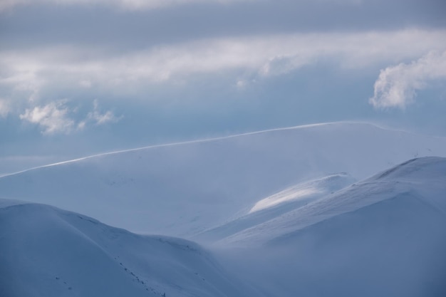 Snow covered winter mountains in last evening sunlight Magnificent windy dusk on tops above picturesque alpine ski resort