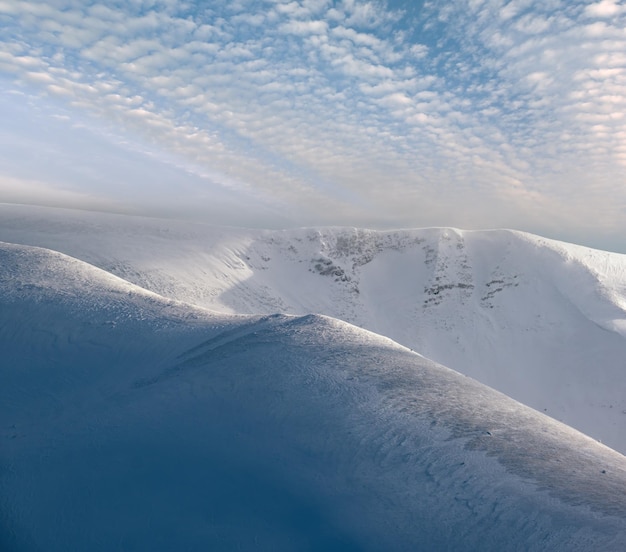 Snow covered winter mountains in last evening sunlight Magnificent windy dusk on tops above picturesque alpine ski resort