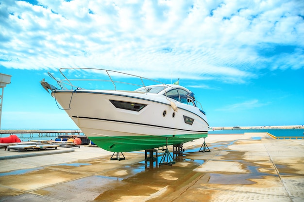 A snow white yacht stands on a pier on coasters on a Sunny day against a beautiful sky with clouds