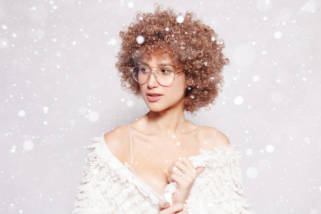 Snow, winter, christmas, people, beauty concept- Portrait of smiling young black woman. Portrait of a beautiful young woman with African American afro haircut wearing eyeglasses over snow background