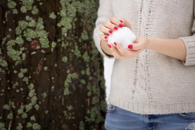 Snowball in hands of a young woman with red manicure and warm sweater Winter walks outdoors