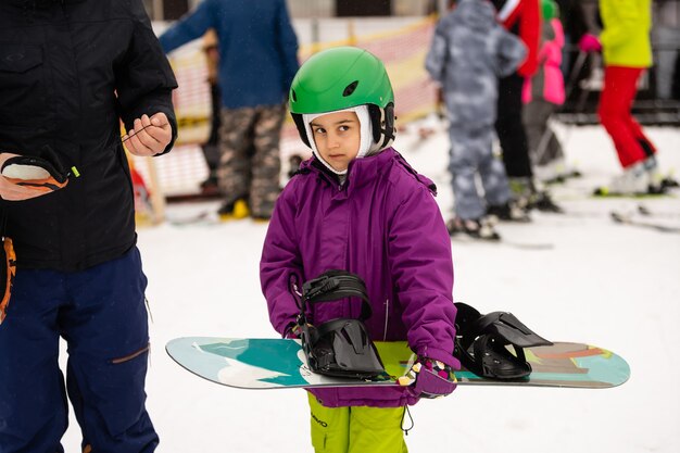 Snowboard Winter Sport. little girl learning to snowboard, wearing warm winter clothes. Winter background.