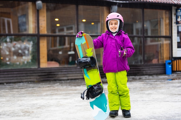 Snowboard Winter Sport. little girl learning to snowboard, wearing warm winter clothes. Winter background.