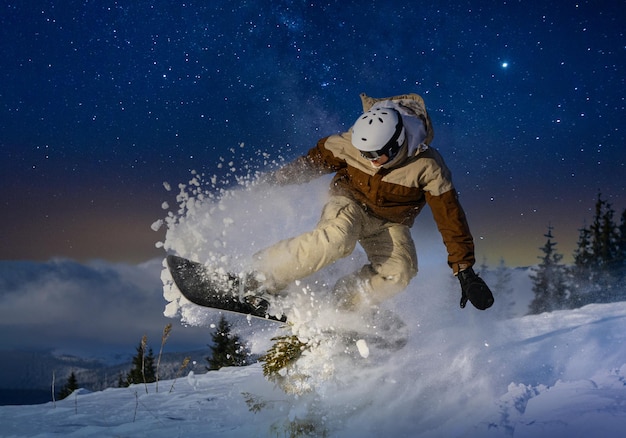 Snowboarder doing freestyle trick against of beautiful mountains under the night starry sky