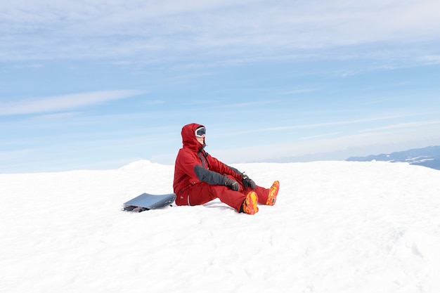 Snowboarder sits high in the mountains on the edge of the slope and looks into the distance