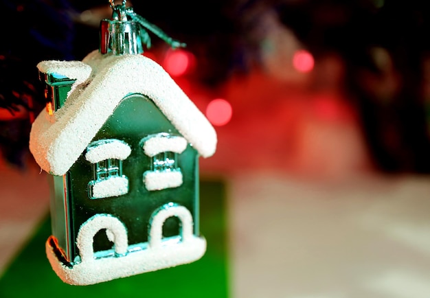 Snowcovered Green Little House Ornament with Red Christmas Decorating Light Bokeh in background