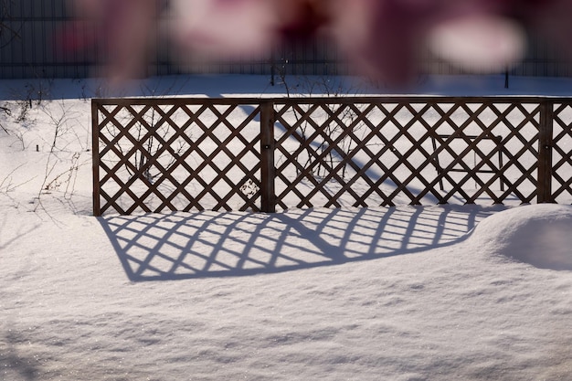 Snowcovered meadow with dry branches and grass and garden fence