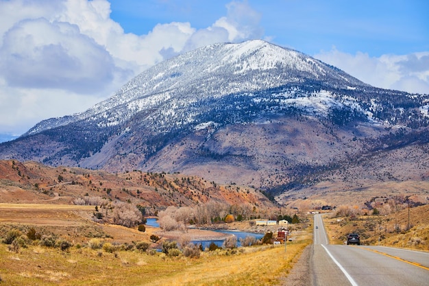 Snowcovered mountains overpowering small paved road leading towards them