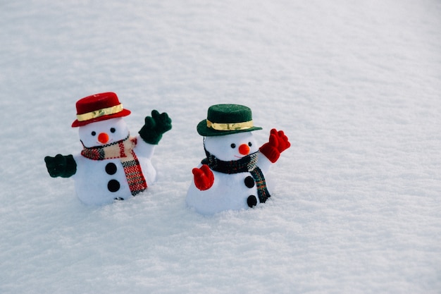 Snowman and friend stand among pile of snow in park. Morning sunshine is warming in winter. Welcome christmas season.