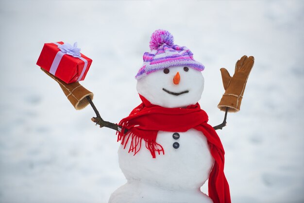 Photo snowman in a scarf and hat. cute snowmen standing in winter christmas landscape. funny snowman in