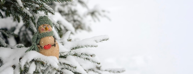 Snowman, toy on the background of a snowy Christmas tree. Snowing. Selective focus, blurred winter background. The concept of the coming New Year.