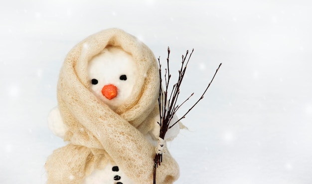 A snowman in a white scarf on a light background holds a broom