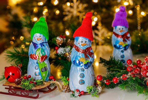 Snowman with sled stands in front of Christmas tree made of milk chocolate